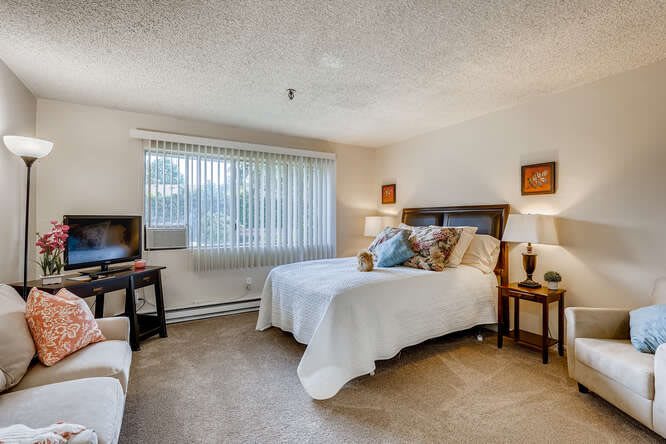 A cozy bedroom with a large window, featuring a comfortable bed and warm decor.