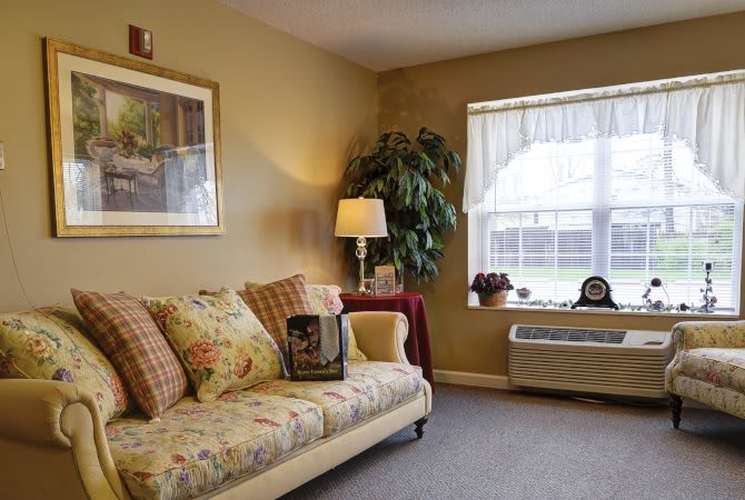 A cozy living room with a sofa, decorative pillows, a lamp, and a window overlooking the outdoors.
