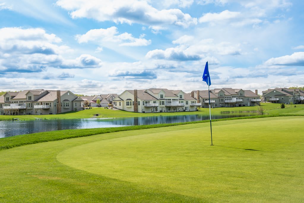 A scenic view of a golf course with a lake and houses in the background.