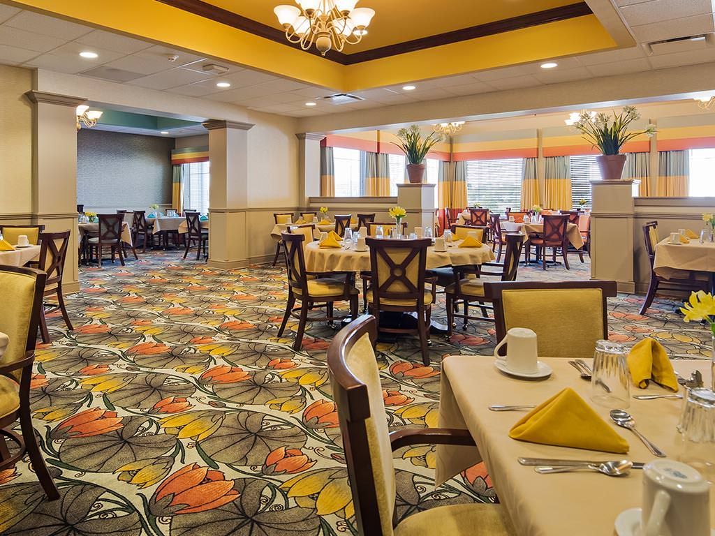 An elegantly designed dining room with multiple tables and chairs, featuring a colorful carpet and chandelier lighting.