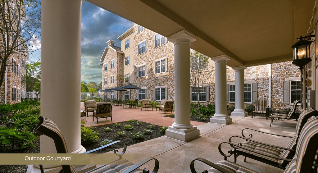 A view of a courtyard with a stone building, featuring columns and outdoor seating.