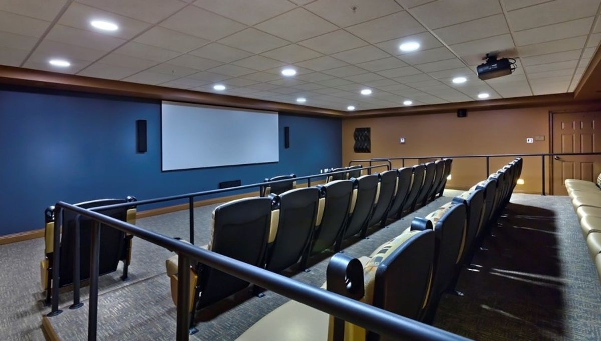 An empty theater with rows of seats facing a large screen.