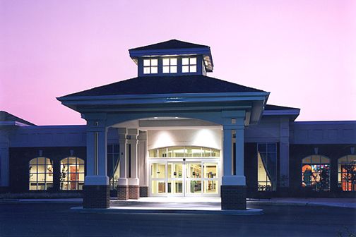 An illuminated building entrance at twilight with a prominent portico.