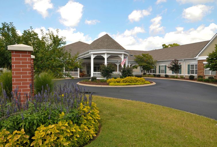 A building with a landscaped entrance and driveway under a partly cloudy sky.