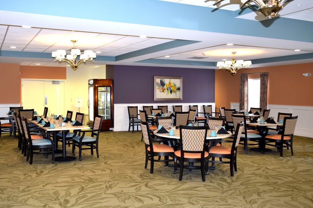 A spacious dining area with neatly arranged tables and chairs, elegant chandeliers, and a colorful wall painting.