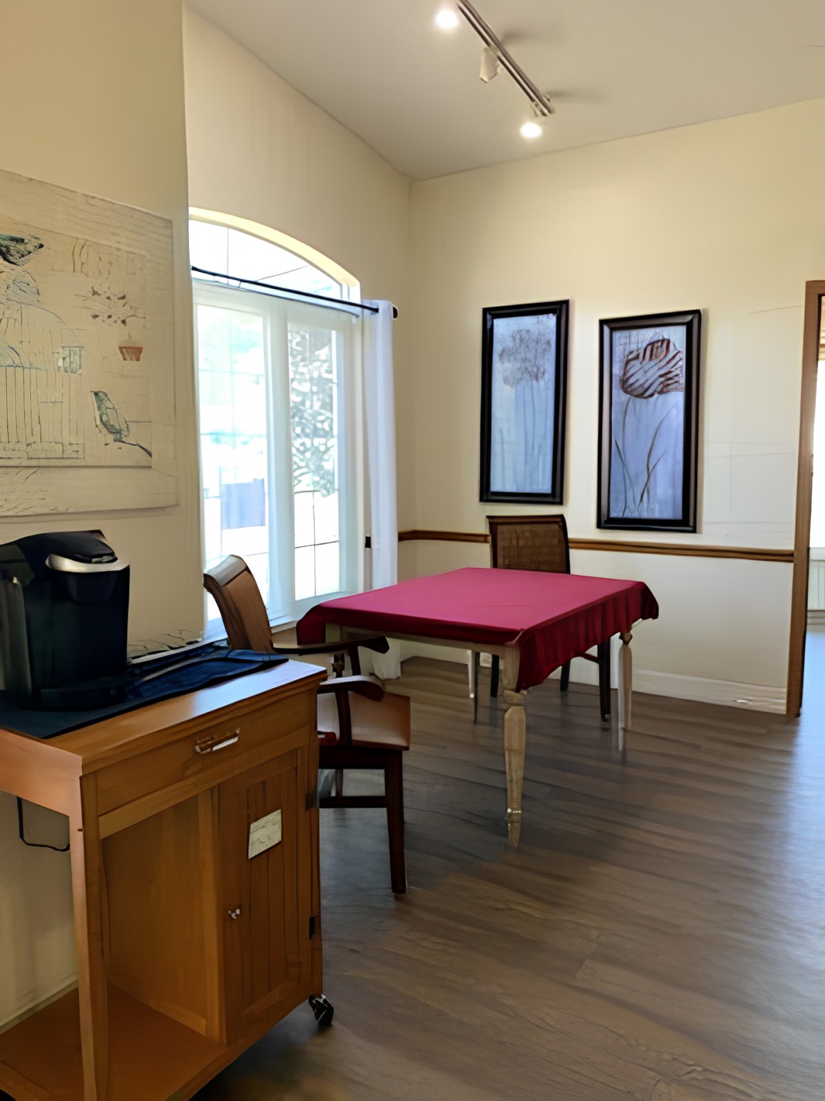A cozy dining area with a table set for two, featuring artwork on the walls and a coffee machine nearby.