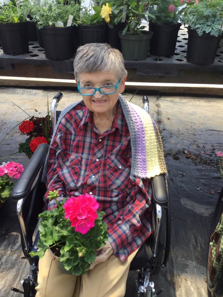 A person in a wheelchair holding a vibrant pink flower in an outdoor garden setting.