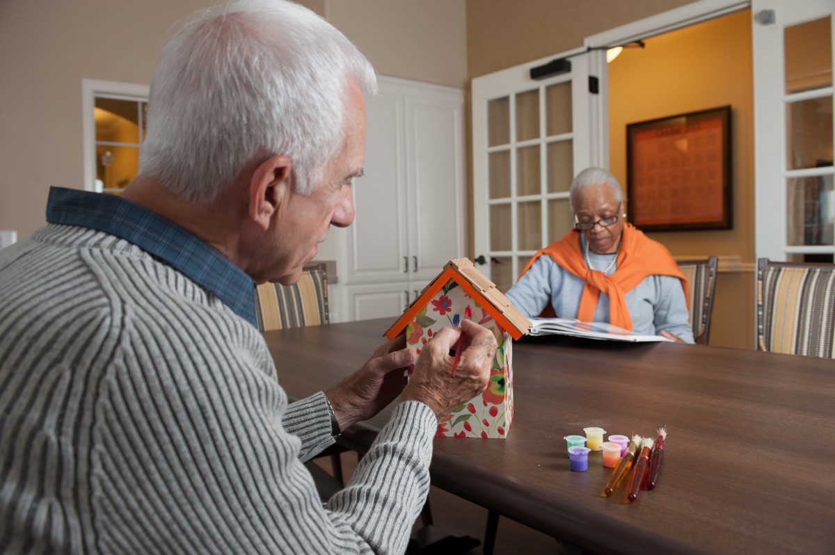 Two seniors engaging in a birdhouse painting activity at a table indoors.