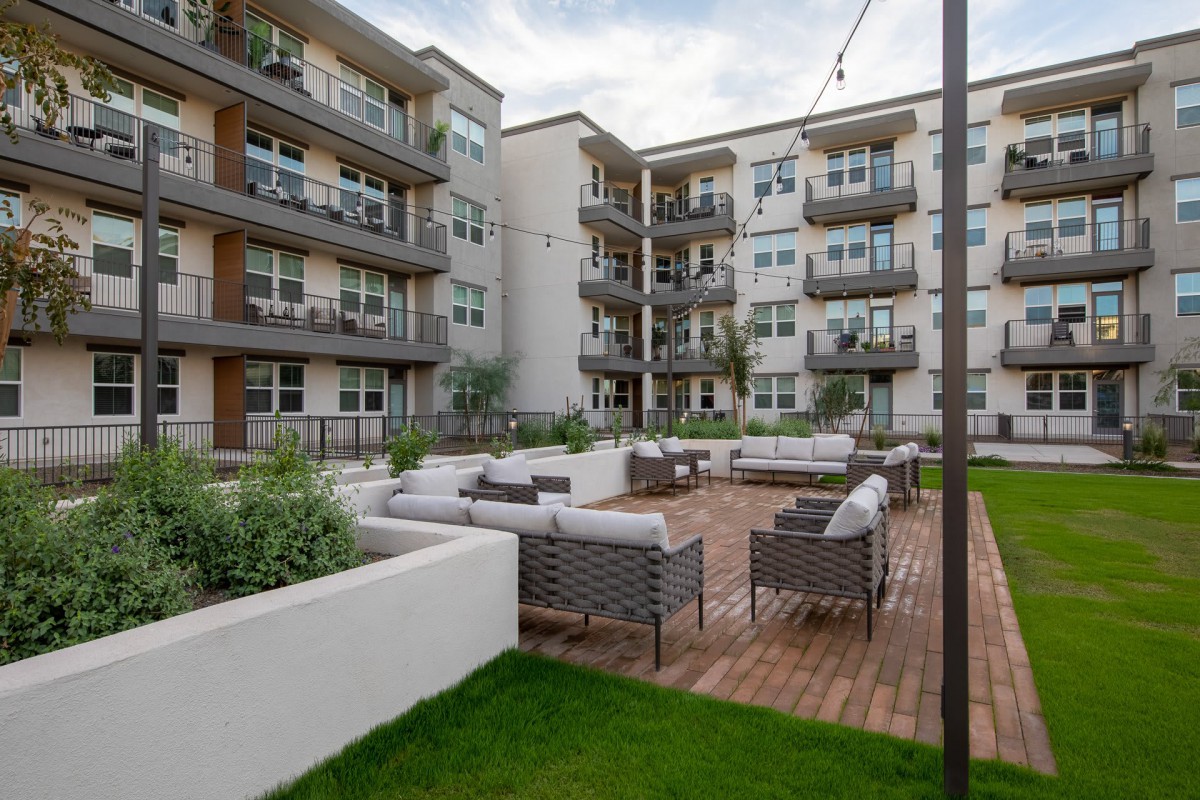 A modern apartment complex features an inviting outdoor patio area with comfortable seating and lush greenery.