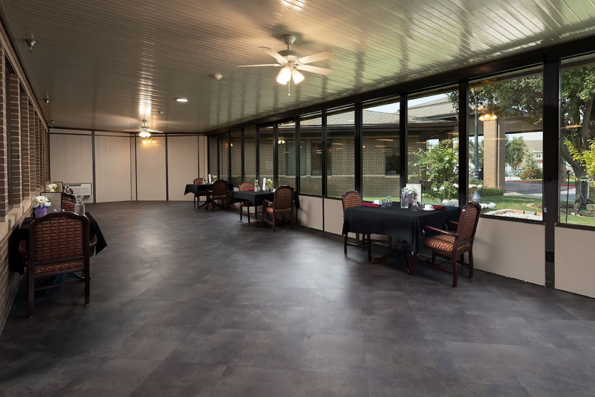 A spacious dining area with tables and chairs, featuring large windows and a ceiling fan.
