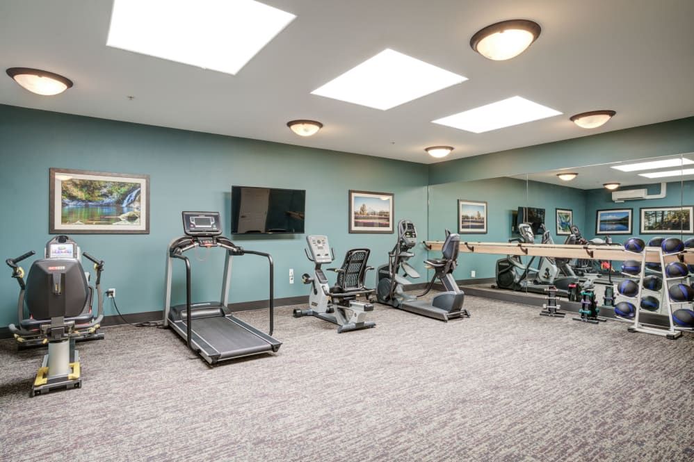 A clean, well-lit gym with exercise equipment including a treadmill and stationary bikes.
