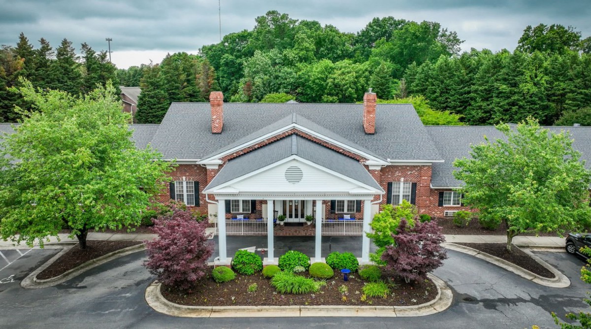 A classic brick building with a prominent entrance surrounded by lush greenery.