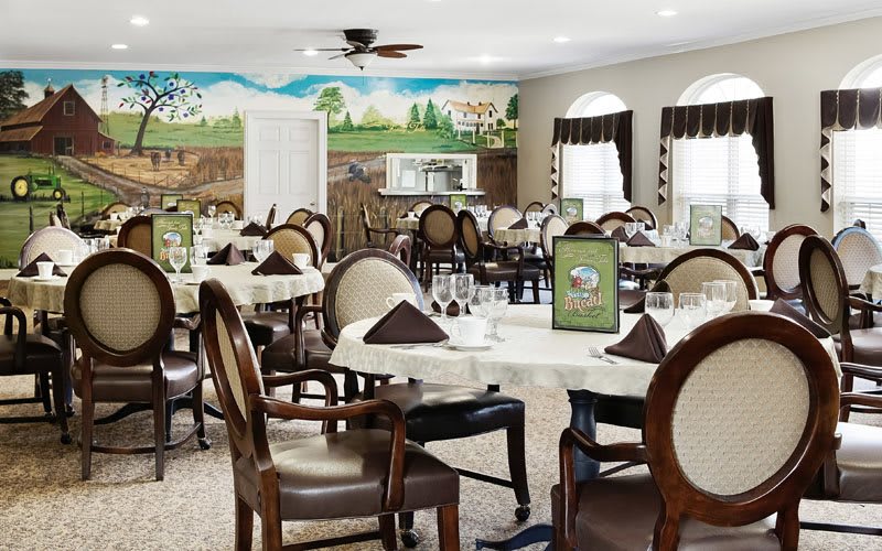 A beautifully decorated dining room with neatly arranged tables and chairs, featuring a scenic mural on the wall.