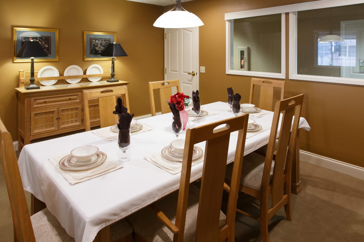 A warmly lit dining room featuring a neatly set table with wooden chairs and decorative elements.
