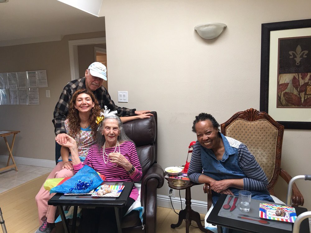 A group of people celebrating indoors, with a focus on an elderly woman wearing a festive bow.