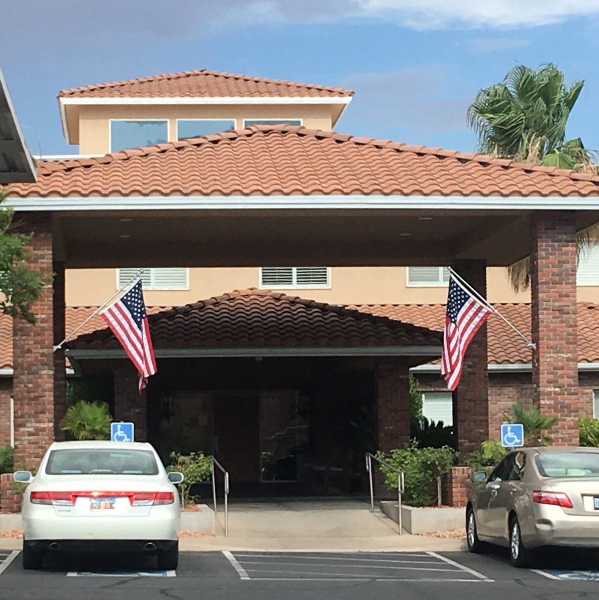 Entrance of a building with American flags and cars parked in front.