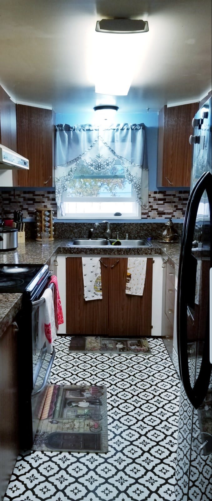 A modern kitchen with wooden cabinets, a stone countertop, and patterned curtains above the window.