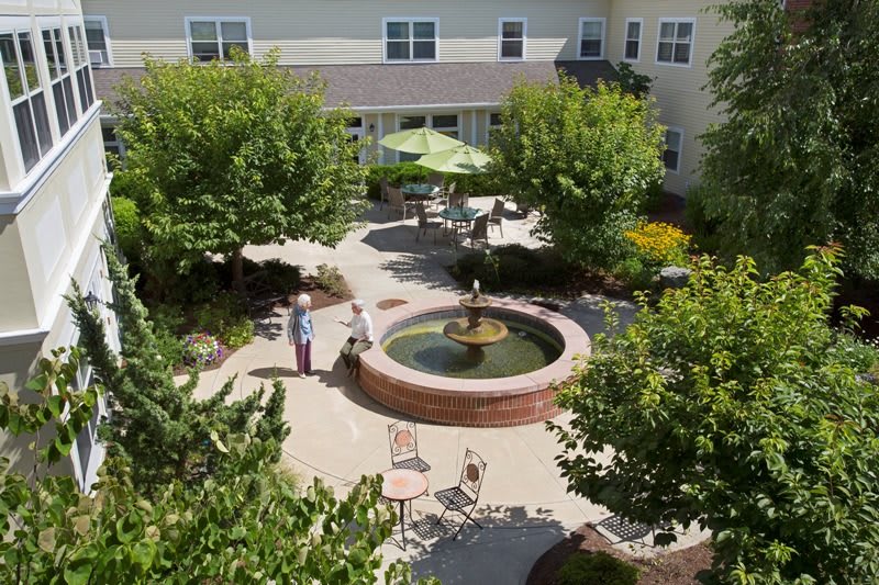 A peaceful courtyard with a central fountain surrounded by lush trees and outdoor seating.