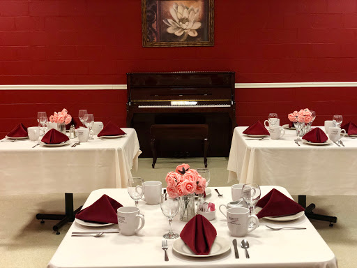 An elegantly arranged dining room featuring tables set for a special occasion, accented by floral arrangements and a classic piano.