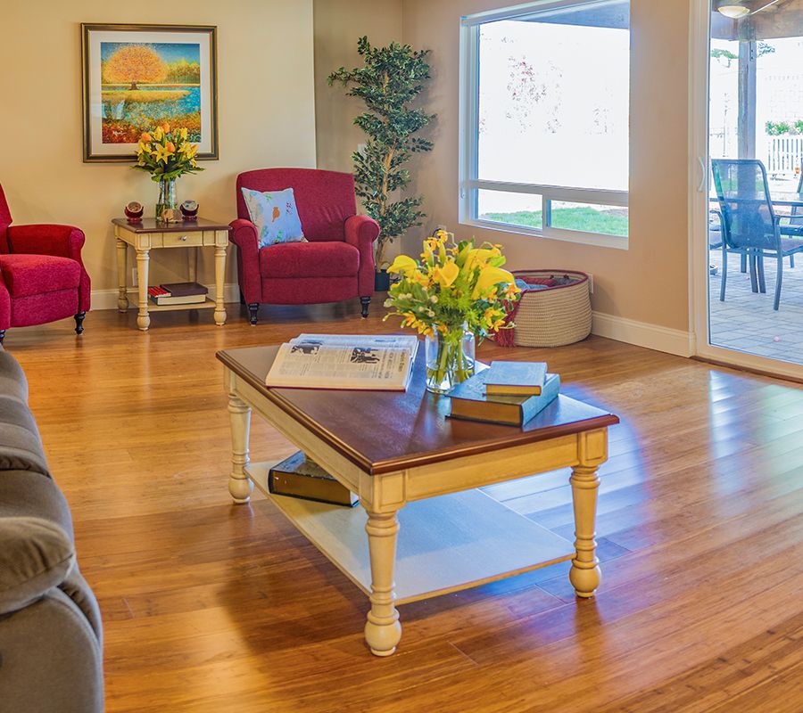 A cozy living room with hardwood floors, a coffee table adorned with flowers, and natural light streaming through the windows.