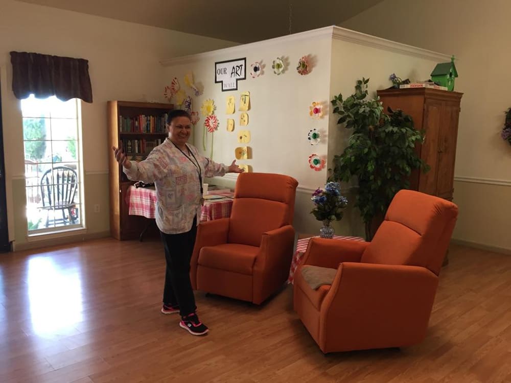A person stands in a cozy living room with orange chairs and colorful decorations.