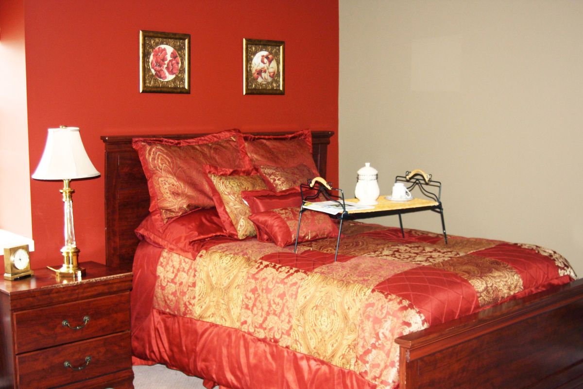 A luxurious bedroom with red and gold bedding, complemented by decorative wall art.