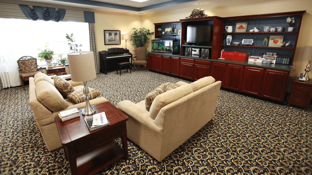 A cozy living room featuring a plush sofa, patterned carpet, and an entertainment center with a piano in the corner.