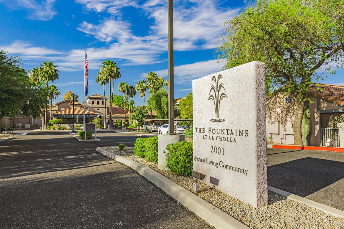 Entrance to a retirement community with palm trees and a clear blue sky.