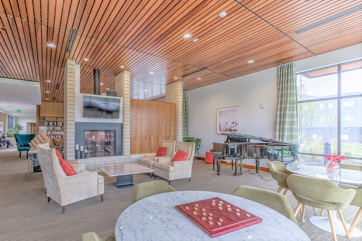 A modern living room with a wooden ceiling, comfortable seating around a fireplace, and a chessboard on the table.
