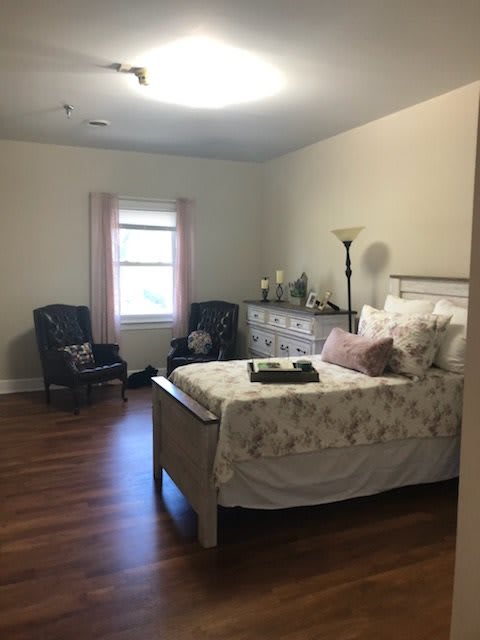 A cozy bedroom with a bed, dresser, and two chairs by the window.