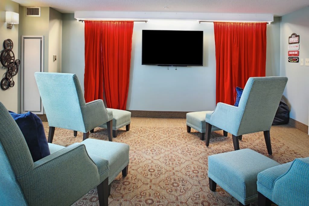 A modern living room with light blue chairs and red curtains facing a wall-mounted TV.