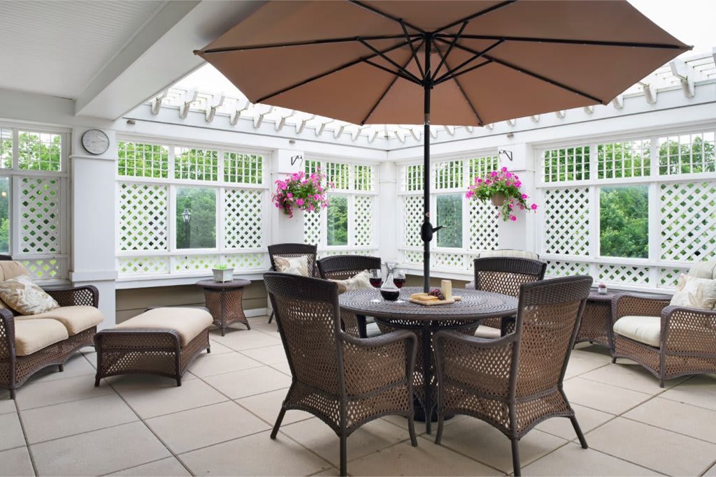 A cozy outdoor patio with a table, chairs, and an umbrella, surrounded by a lattice fence adorned with hanging flower baskets.