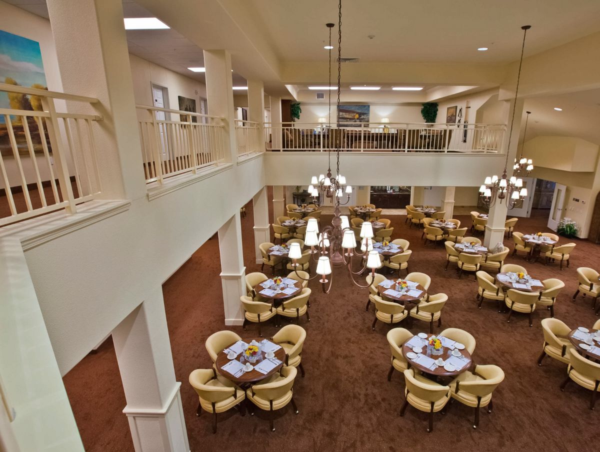 An elegant indoor dining area with multiple tables and chairs, featuring large chandeliers.