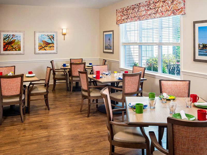 A well-decorated dining room with neatly arranged tables and chairs, featuring large windows that let in natural light.