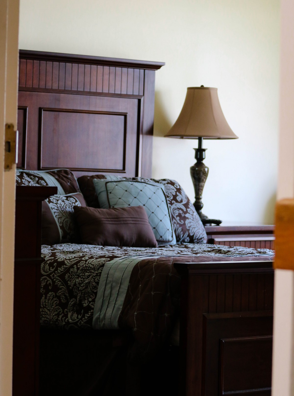 A cozy bedroom with a wooden headboard, decorative pillows, and a bedside lamp.
