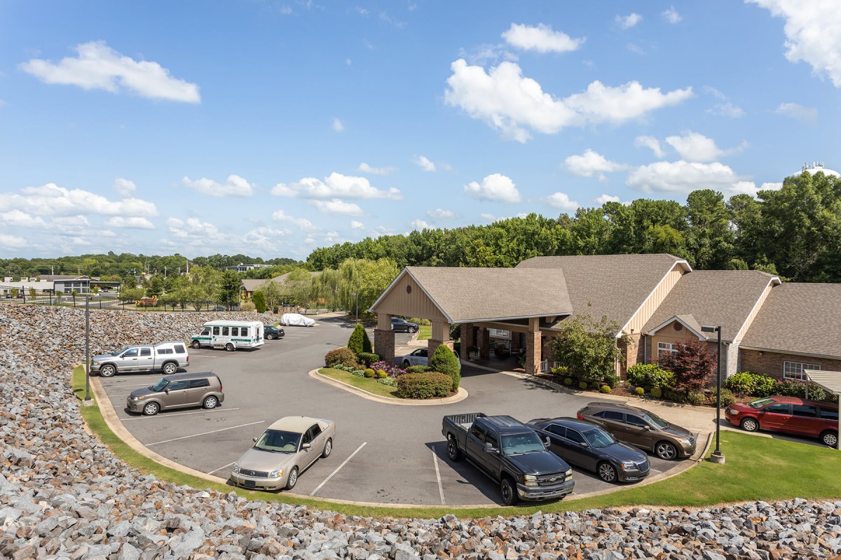 A suburban building with a surrounding parking lot full of cars under a partly cloudy sky.