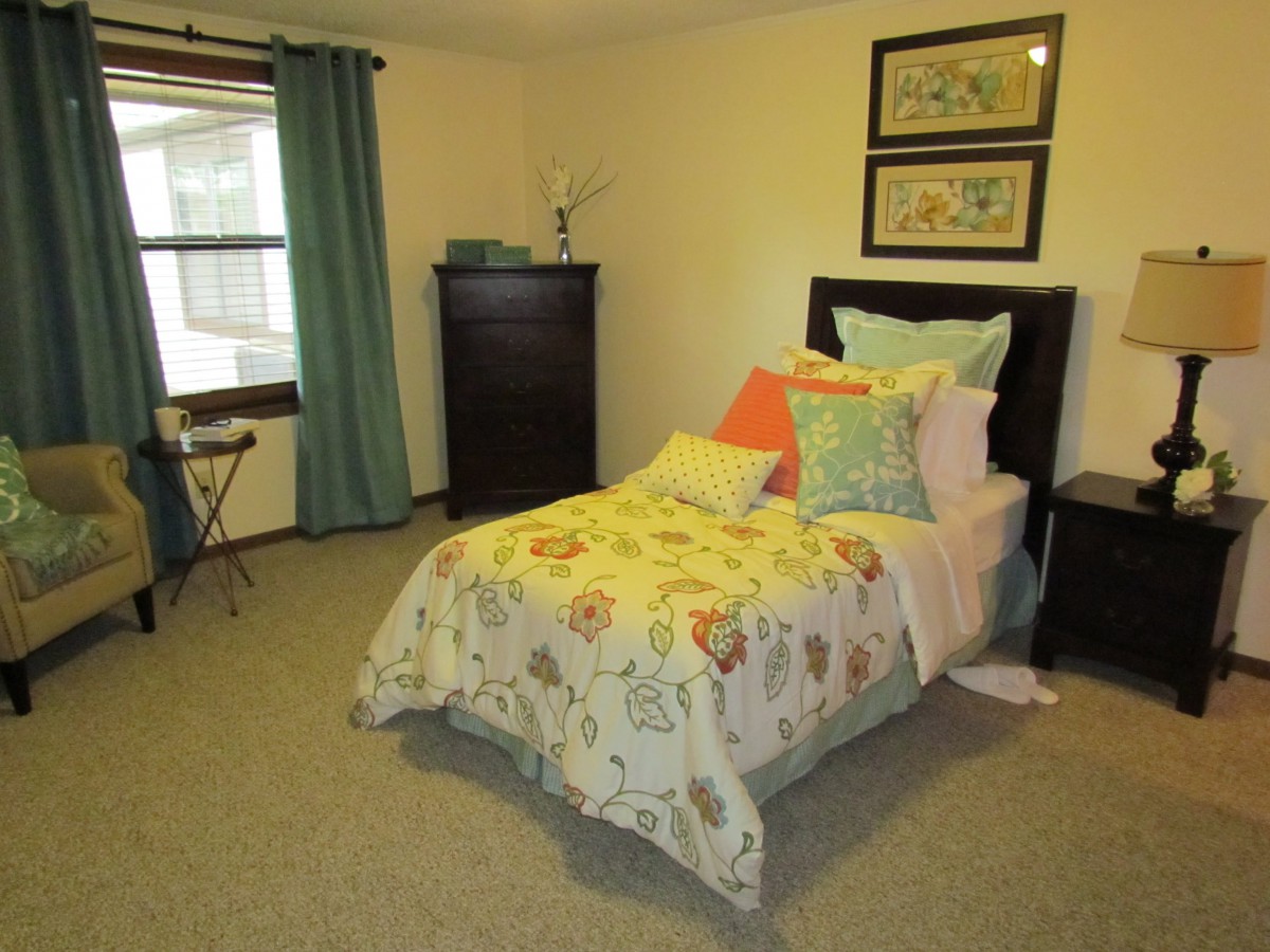 A cozy bedroom with a neatly made bed featuring colorful pillows and a floral-patterned comforter.
