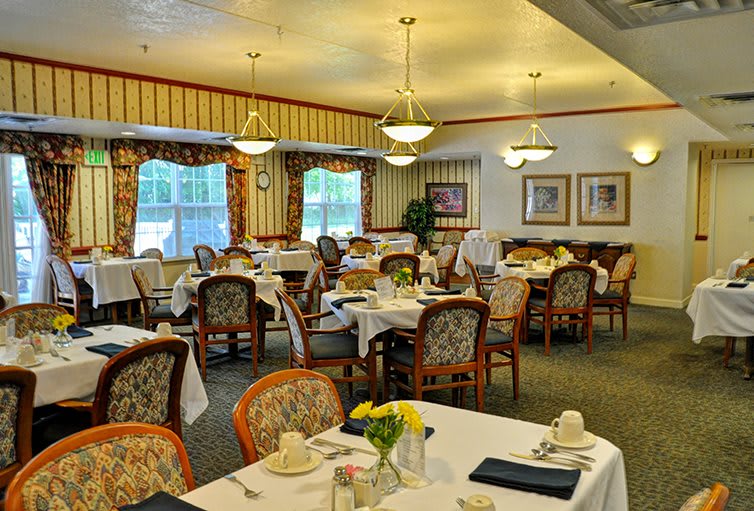 An elegant dining room with neatly arranged tables and chairs, featuring chandeliers and tasteful decor.