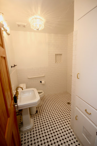 A clean and minimalist bathroom featuring white tiles and a classic black and white floor pattern.