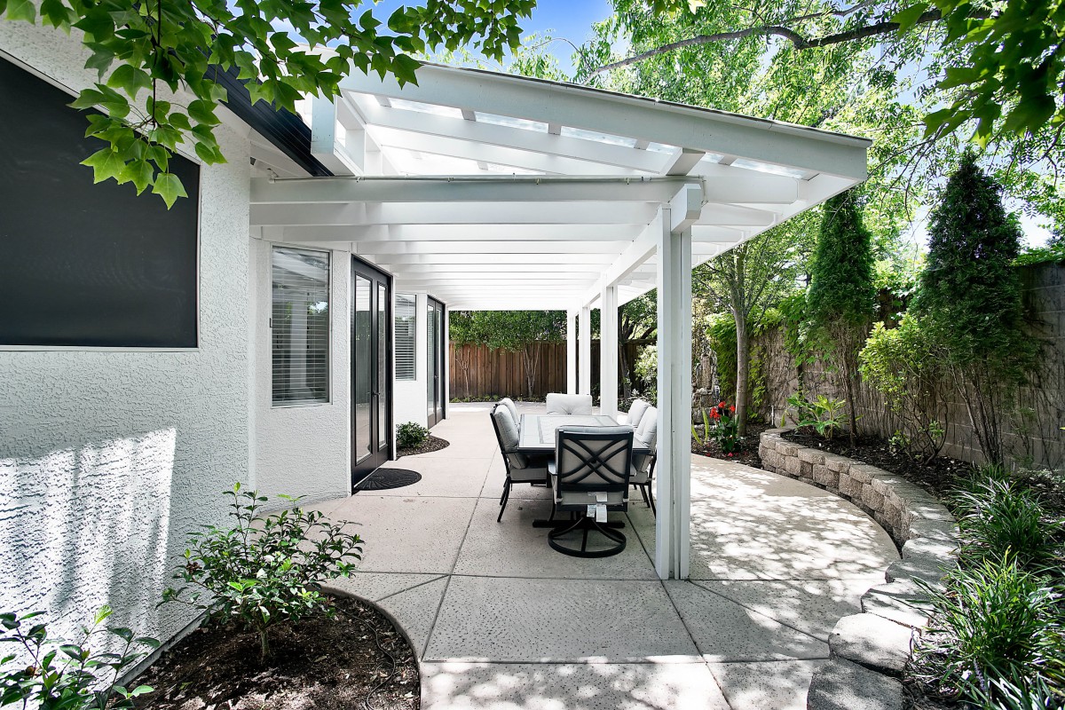 A modern patio with a pergola and outdoor dining set in a garden setting.
