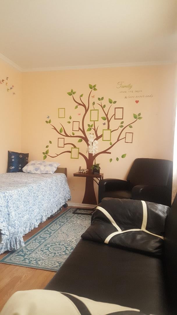 A cozy bedroom with a tree mural featuring empty photo frames on the wall, alongside a bed and an armchair.