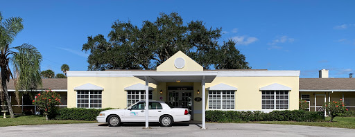A white taxi parked in front of a yellow building with a welcoming entrance.
