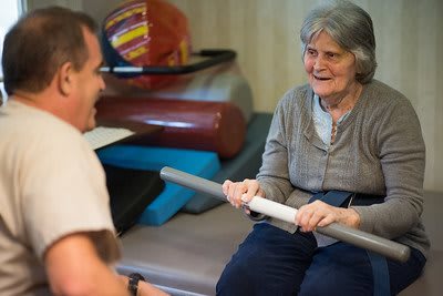 An elderly woman participating in a physical therapy session, engaging in exercises with support.