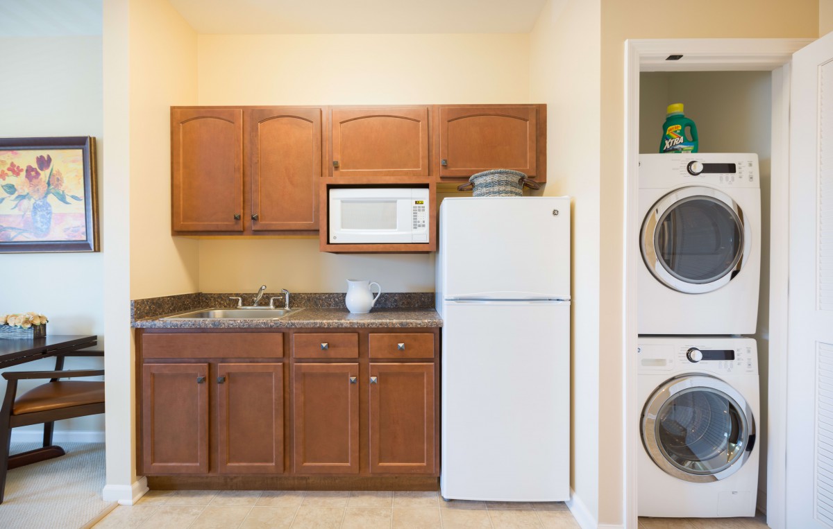 A compact kitchen with wooden cabinets, a microwave, refrigerator, and an adjacent stacked washer and dryer.