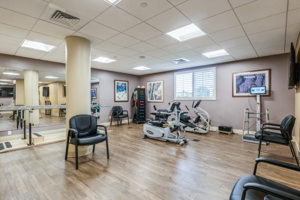 A well-lit indoor gym with exercise machines and chairs.