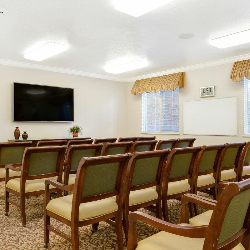 A neatly arranged conference room with rows of chairs facing a large television.