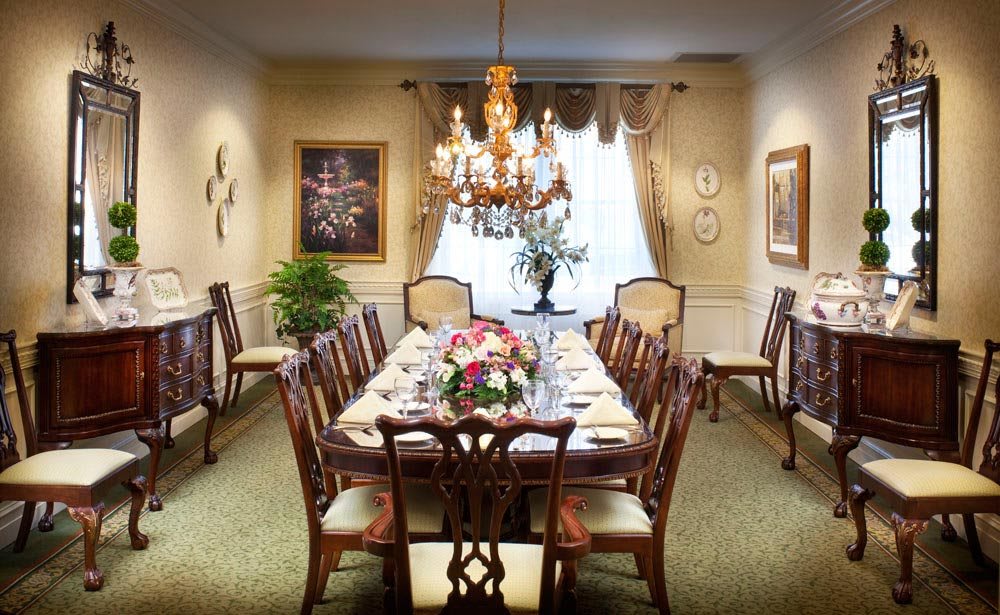 A beautifully furnished dining room with a long table set for a formal dinner, decorated with a floral centerpiece and illuminated by an elegant chandelier.