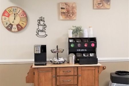 A neatly organized coffee station with a machine, cups, and decor on a wooden cabinet.
