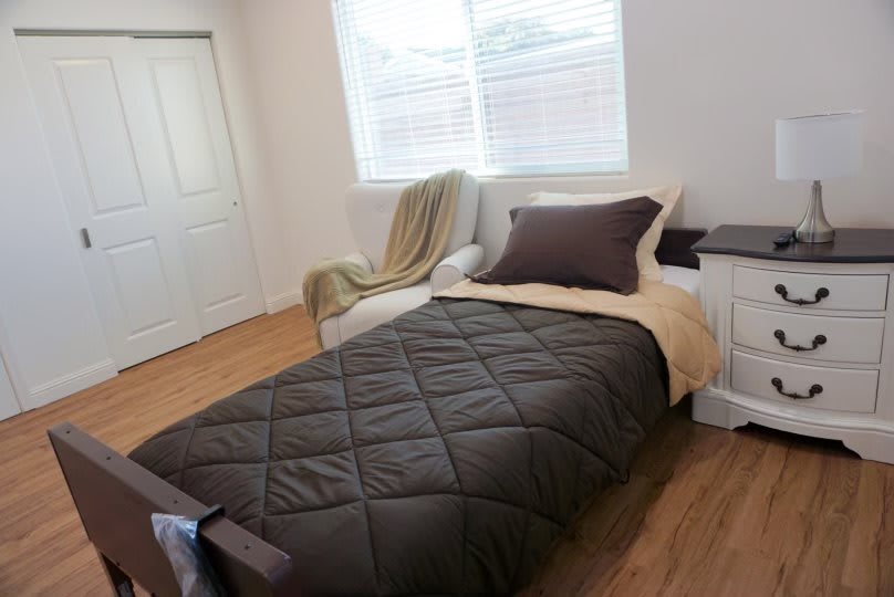 A minimalist bedroom with a single bed, wooden flooring, and natural light from a window.