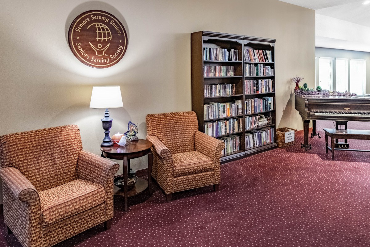 A cozy reading area with armchairs, a lamp, and a bookshelf full of books.